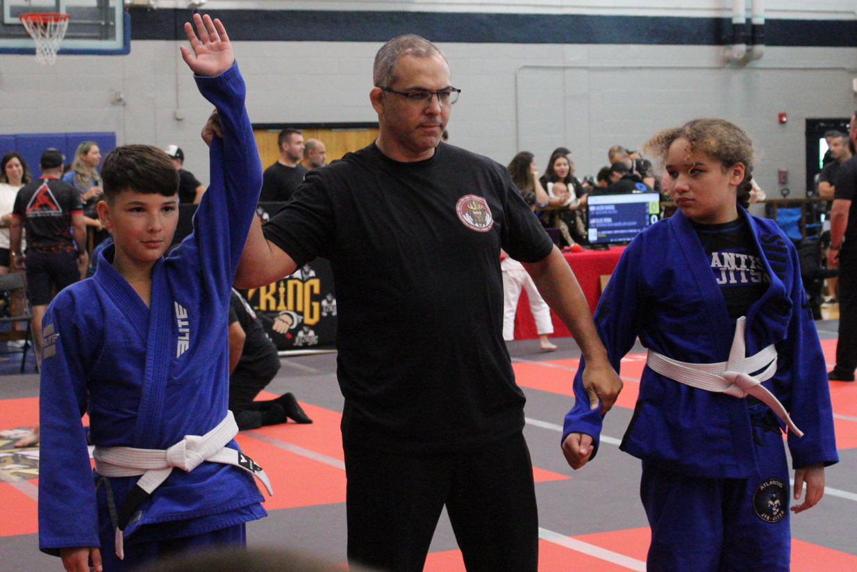 Referee raising a young jiu-jitsu competitor's hand after a win in the kids gi division
