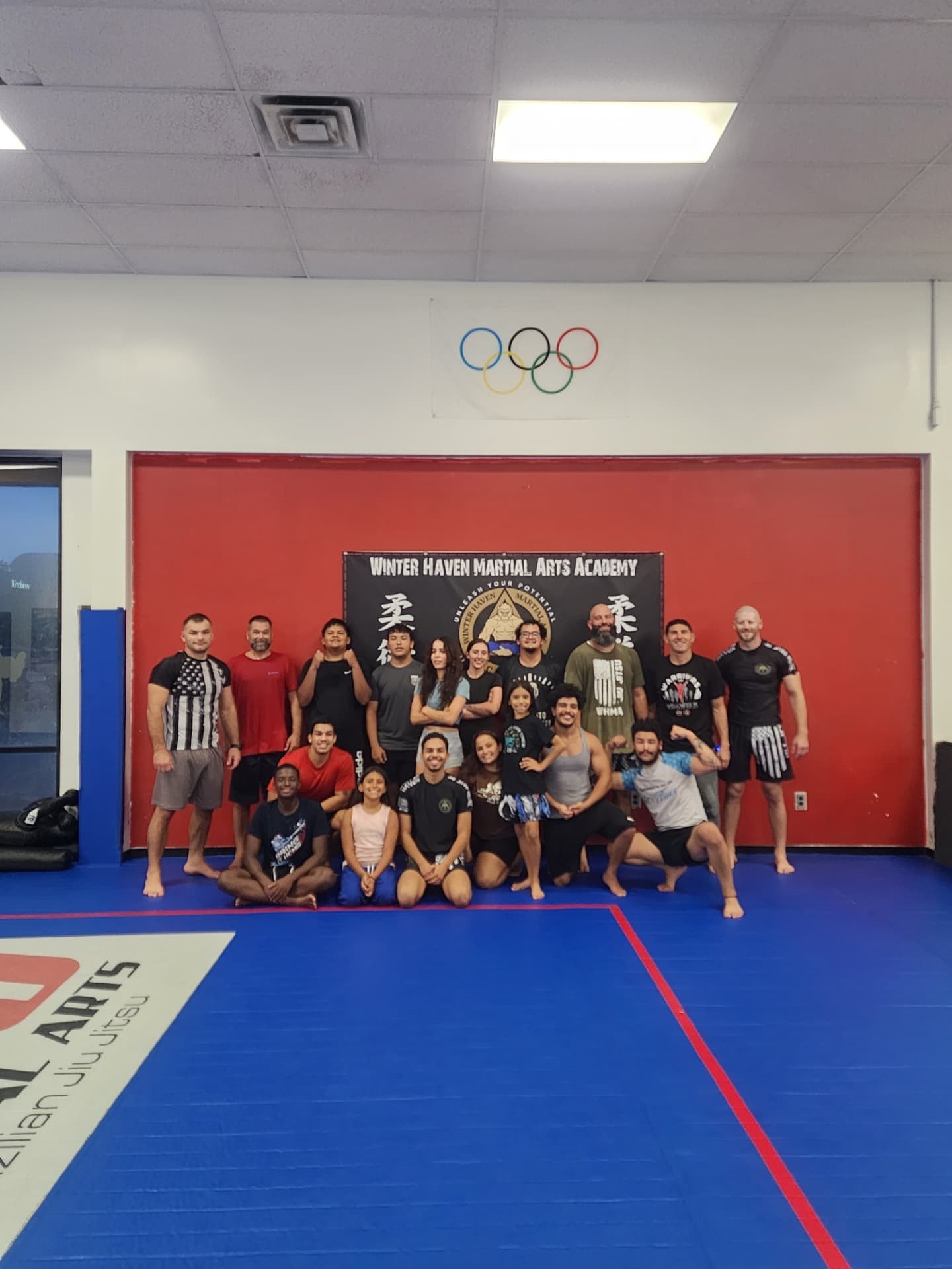 Adult and teen students group photo in front of the Winter Haven Martial Arts Academy banner and Olympic rings