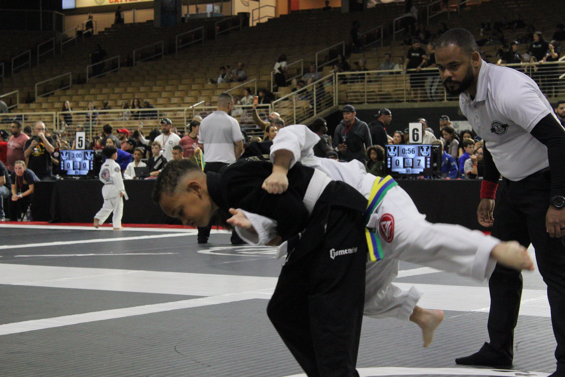 Kids gi jiu-jitsu takedown in progress during a tournament match
