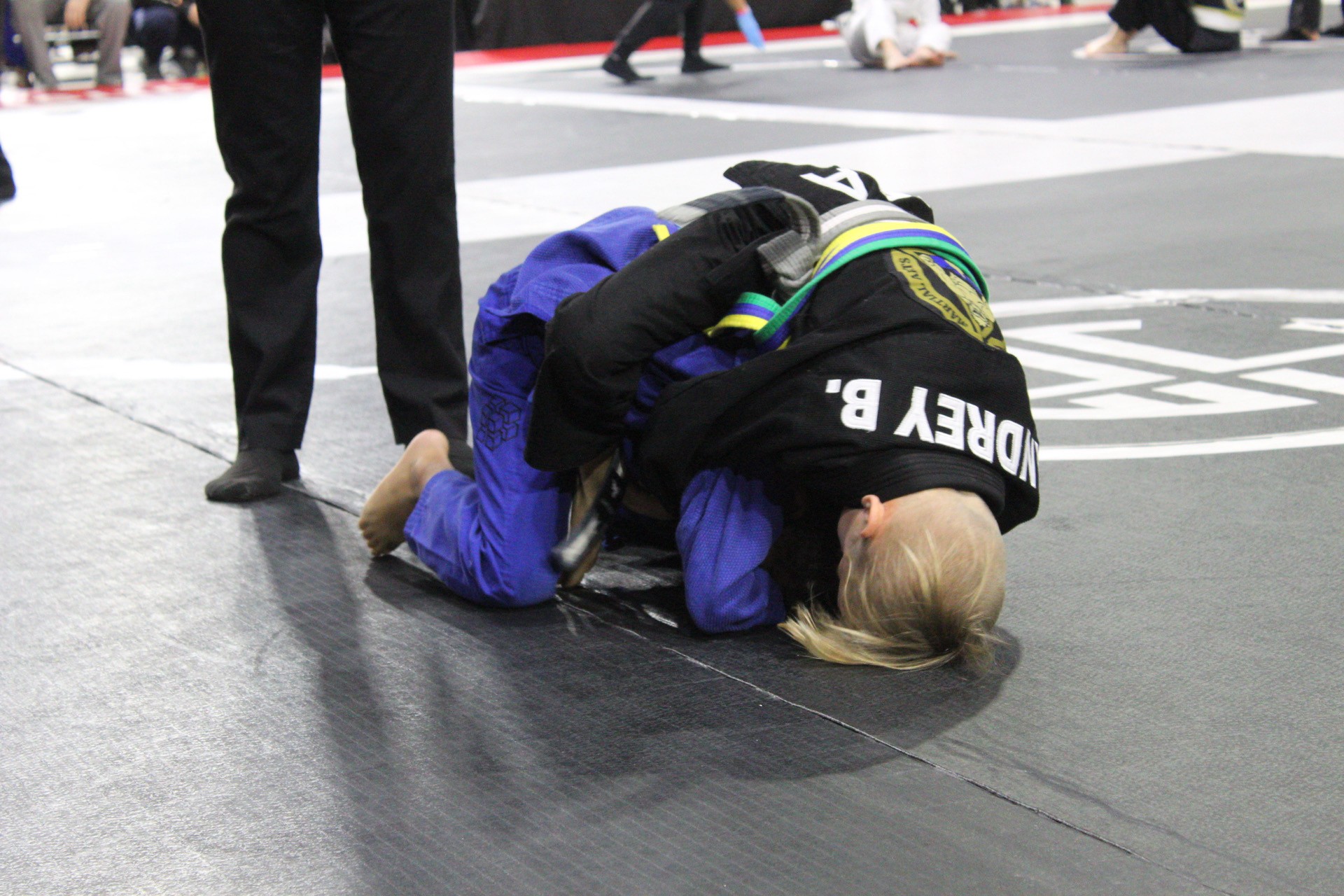 Kids gi jiu-jitsu groundwork during a tournament match on the mats
