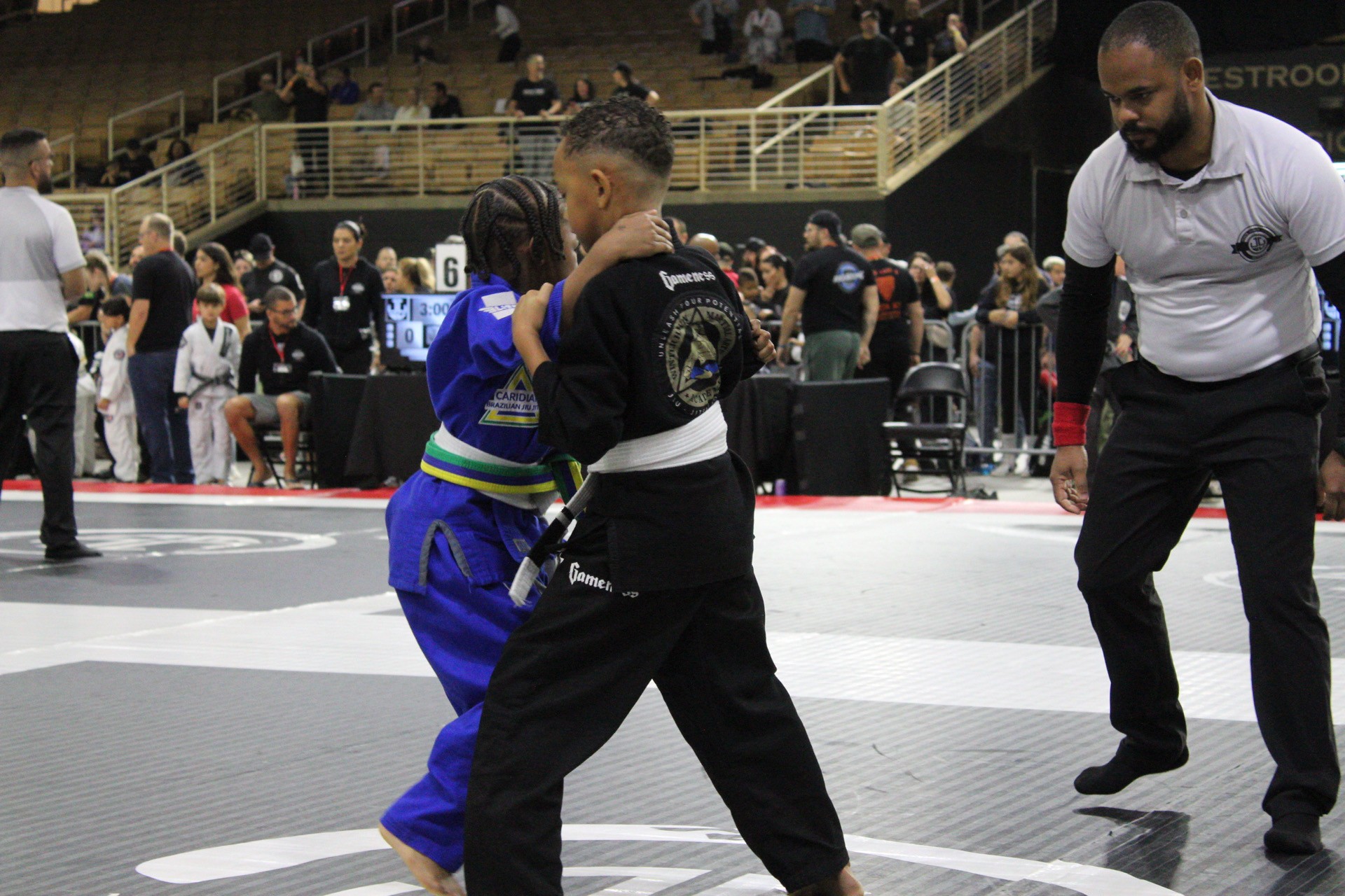 Two kids grip fighting at the start of a gi jiu-jitsu match as the referee watches
