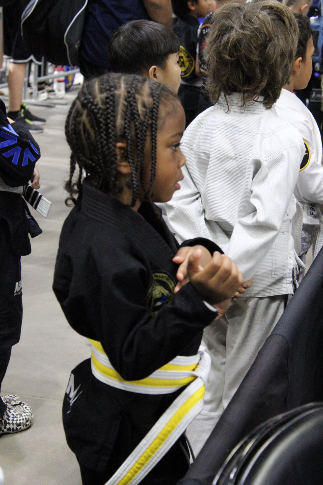 Young jiu-jitsu competitors in gis waiting matside for their matches at a tournament