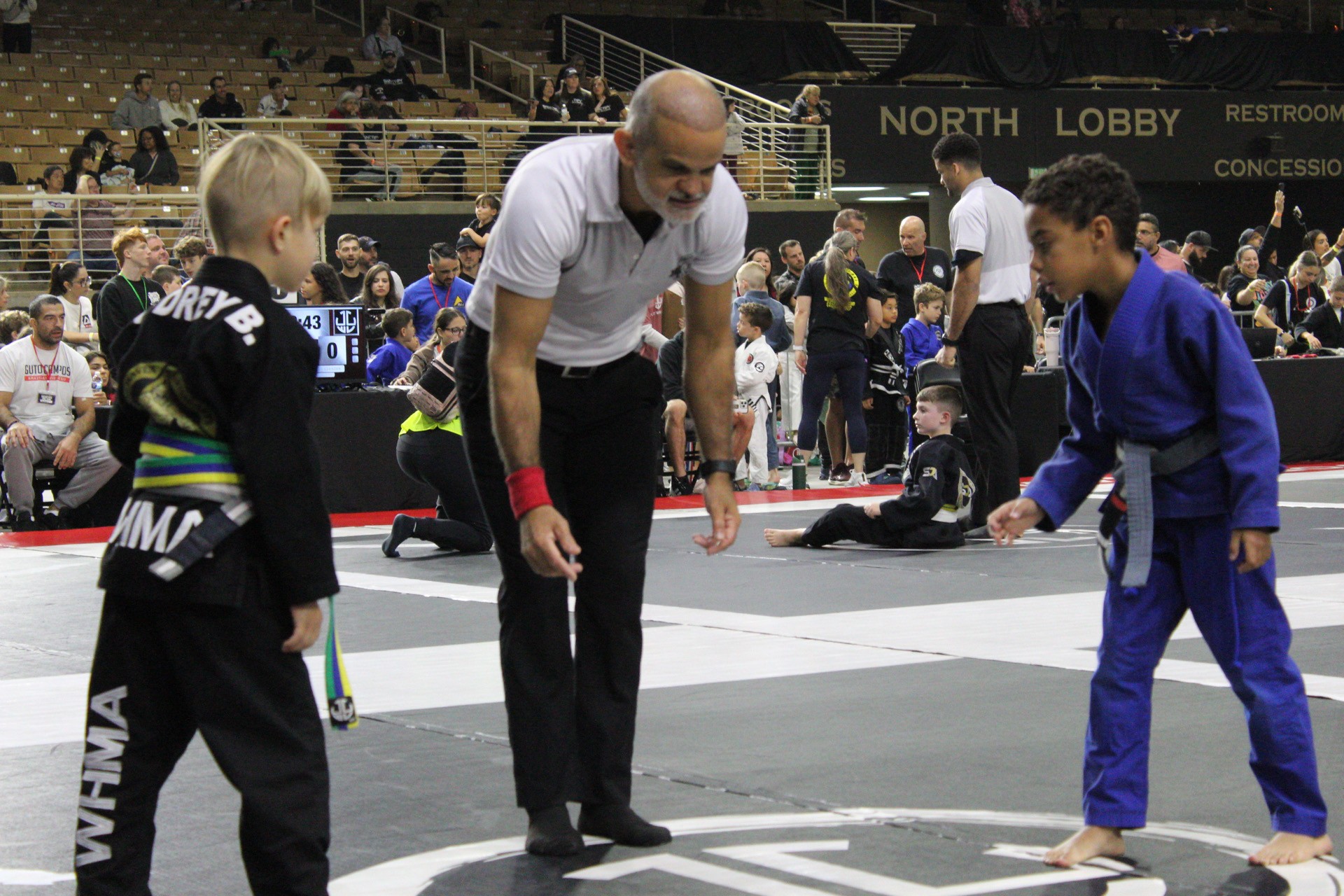 Referee starting a kids gi jiu-jitsu match between two young competitors